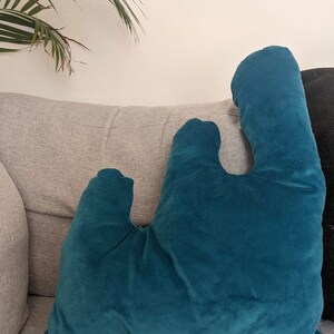 Könnte beinhalten: Ein blaues Samtkissen in Wellenform. Das Kissen liegt auf einem grauen Sofa.