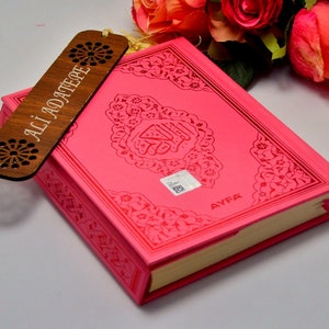 Può includere: Un libro rosa con disegni in rilievo e pagine dorate, accompagnato da un segnalibro in legno. Il segnalibro presenta motivi floreali traforati e il testo "ALI ADATEPE".