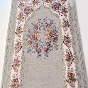 May include: A rectangular prayer rug featuring a light gray background with a central arch design. The rug is decorated with intricate floral patterns in shades of pink, blue, yellow, and green, framed by ornate borders with detailed scrollwork.