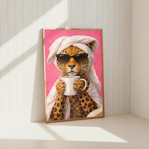 May include: A framed art print featuring a leopard wearing sunglasses and a white towel on its head, holding a white coffee mug. The leopard has a spotted coat and is set against a pink background.