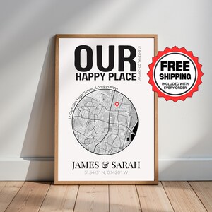 May include: A framed print with the words "OUR HAPPY PLACE" in large black letters. Below is a map of an area with a red marker. The names "JAMES & SARAH" are printed at the bottom. The print is in a wooden frame.
