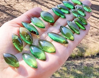 Puede incluir: Una colección de 17 piezas de ámbar verde en forma de hoja, algunas con inclusiones, mostradas en una mano.