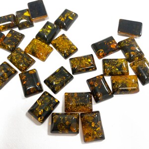 Può includere: Una collezione di cabochon di pietra preziosa ambra in varie tonalità di marrone e giallo. I cabochon sono di forma rettangolare e hanno una finitura liscia e lucida.