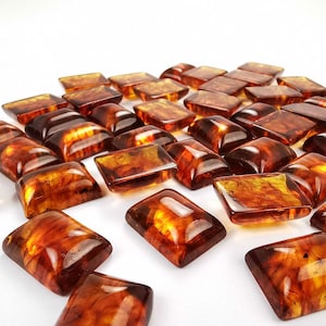 Puede incluir: Una colección de piedras preciosas de ámbar, cortadas en formas rectangulares, con una variedad de tonos de marrón y naranja. Las piedras preciosas están dispuestas en un patrón aleatorio sobre una superficie blanca.