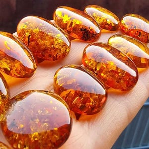 May include: A collection of oval-shaped amber stones with inclusions. The stones are a deep orange color and have a glossy finish.