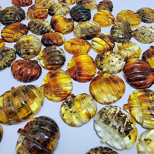 Peut inclure: Une collection de pendentifs en forme de feuille d'ambre dans différentes nuances de jaune, orange et brun. Les pendentifs sont sculptés avec des détails complexes et ont une finition polie.