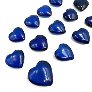 Op de afbeelding: Een assortiment diepblauwe glazen hartvormige kralen. De kralen zijn gerangschikt op een witte ondergrond, met verschillende tinten blauw en highlights. De harten zijn glad en glanzend en reflecteren licht.