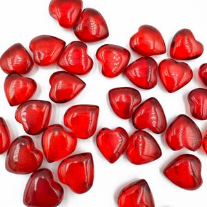 May include: A collection of red glass heart-shaped beads. The beads are scattered on a white surface.