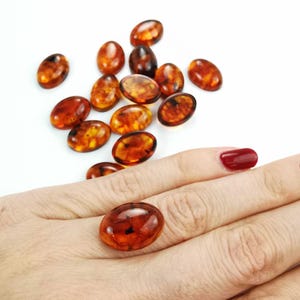 Può includere: Una collezione di pietre preziose di ambra di forma ovale in diverse tonalità di marrone, alcune con inclusiones, esposte su una mano.