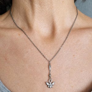 Peut inclure: Collier argenté avec un pendentif abeille. La chaîne délicate descend jusqu'à un petit charme d'abeille détaillé. Le pendentif abeille a des ailes déployées et des détails complexes. Le collier est porté autour du cou.
