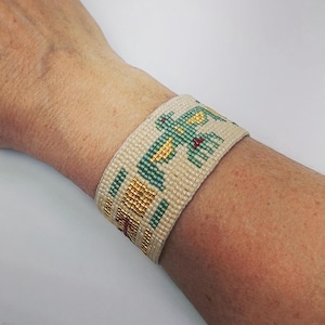 Può includere: Bracciale a polsino con perline color crema, verde acqua, oro e rosso. Il bracciale presenta un motivo geometrico con un disegno a forma di uccello. Il polsino è largo e si avvolge attorno al polso. Le perline sono piccole e fittamente intrecciate.