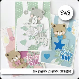 May include: A selection of handmade baby greeting cards. Each card features a teddy bear design on overalls, with details like flowers, hearts, and the words "New Baby," "Baby Girl," and "Baby Boy." The cards are in pastel colours.