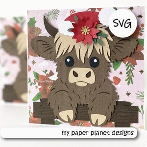 May include: A layered paper craft of a brown Highland cow wearing a red Santa hat with a poinsettia, resting on a dark brown fence. The background features a light pink floral pattern with holly and stars. The text SVG is visible.