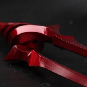 May include: A close-up of a red metal trident with a sharp point. The trident is made of a shiny metal and has a smooth surface.
