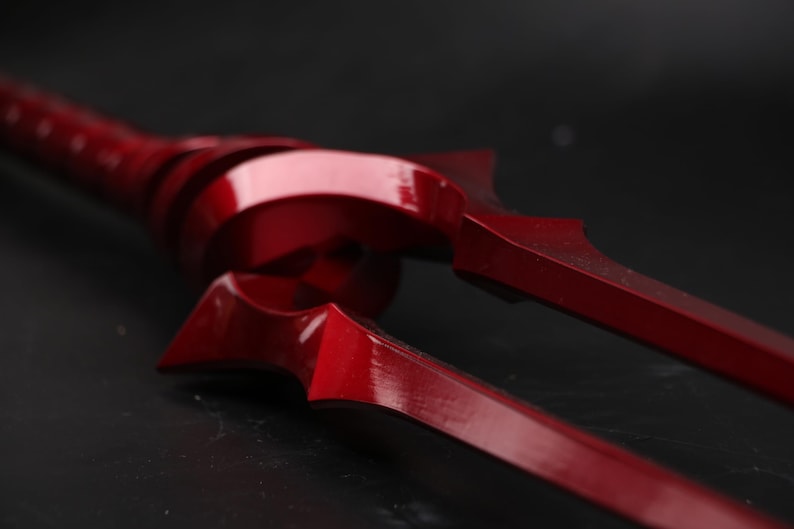May include: A close-up of a red metal trident with a sharp point. The trident is made of a shiny metal and has a smooth surface.