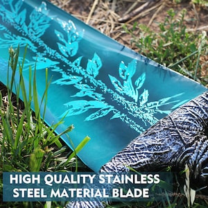 Op de afbeelding: Een close-up van een blauw zwaardblad met een decoratief patroon. De tekst "HIGH QUALITY STAINLESS STEEL MATERIAL BLADE" is zichtbaar onderaan de afbeelding.