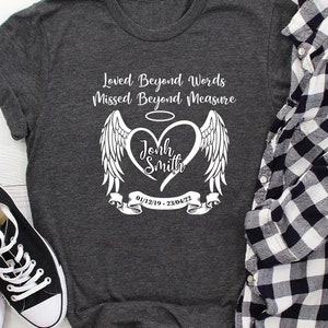 May include: A grey t-shirt with a white graphic of a heart with angel wings. The heart has a halo above it and the text "Loved Beyond Words Missed Beyond Measure" is above the heart. The text "John Smith" is inside the heart and the dates "01/12/19 - 23/04/22" are below the heart.