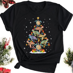 Könnte beinhalten: Schwarzes T-Shirt mit einem Weihnachtsbaumdesign aus Meeresschildkröten. Der Baum ist mit bunten Lichtern und Ornamenten geschmückt.