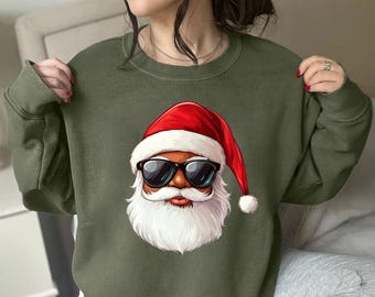 Op de afbeelding: Een groen sweatshirt met een cartoon afbeelding van Sinterklaas met een zonnebril. Sinterklaas heeft een rode muts, een witte baard en een zwarte huid.