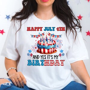 May include: White t-shirt with a colorful graphic celebrating the 4th of July and a birthday. The design features a cake decorated with red, white, and blue, fireworks, and the text "HAPPY JULY 4TH AND YES IT'S MY BIRTHDAY."