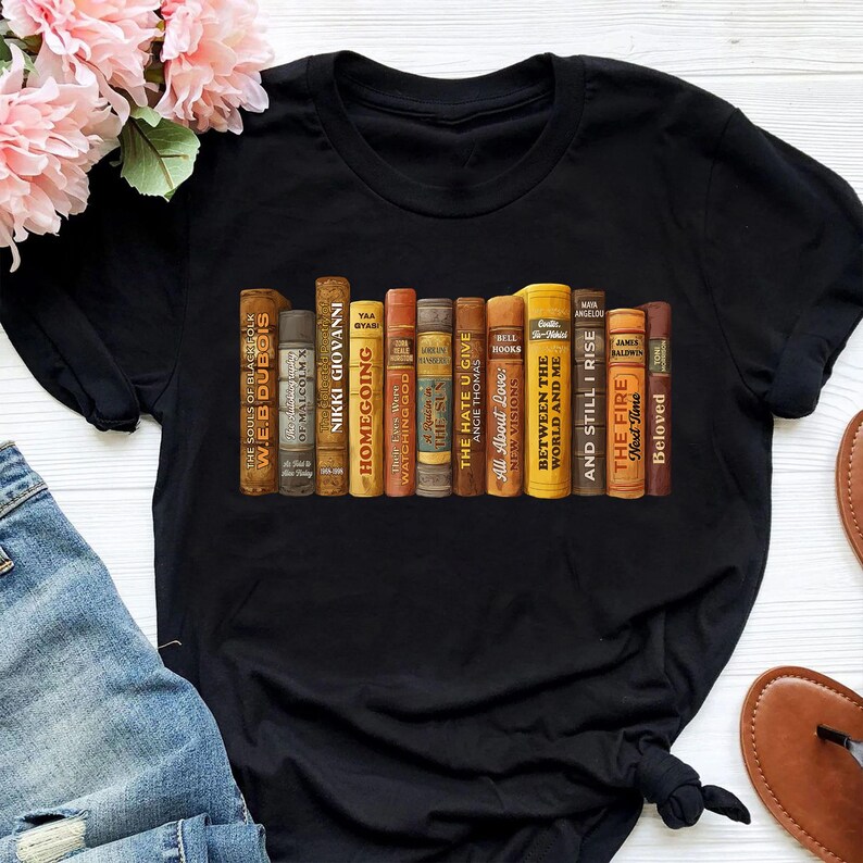 Puede incluir: Camiseta negra con un dise&ntilde;o de una fila de libros antiguos. Los t&iacute;tulos incluyen "Homegoing" y "Between the World and Me". El dise&ntilde;o tiene un tema literario.