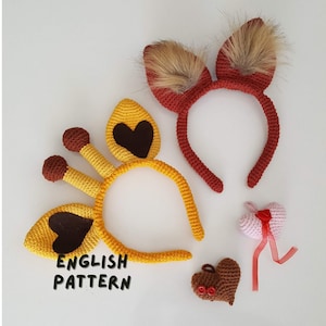 Puede incluir: Diademas y adornos en forma de corazón tejidos a ganchillo. Las diademas incluyen un diseño de jirafa amarilla con detalles marrones y un diseño de orejas de zorro rojas con piel sintética. También se muestran dos corazones tejidos a ganchillo, uno rosa con una cinta roja y otro marrón con botones rojos. El texto "ENGLISH PATTERN" es visible.