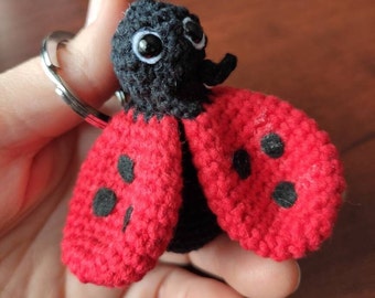 May include: A handmade crochet ladybug keychain. The ladybug has a black head and body, with bright red wings featuring black spots. The keychain is attached to a silver metal ring.