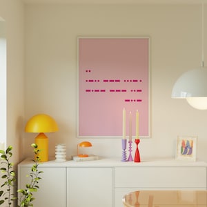 Op de afbeelding: Een roze ingelijste poster met een roze achtergrond en een patroon van magenta stippen en streepjes. Voor de poster staan drie kandelaars met witte kaarsen. De kandelaars zijn paars, blauw en rood.