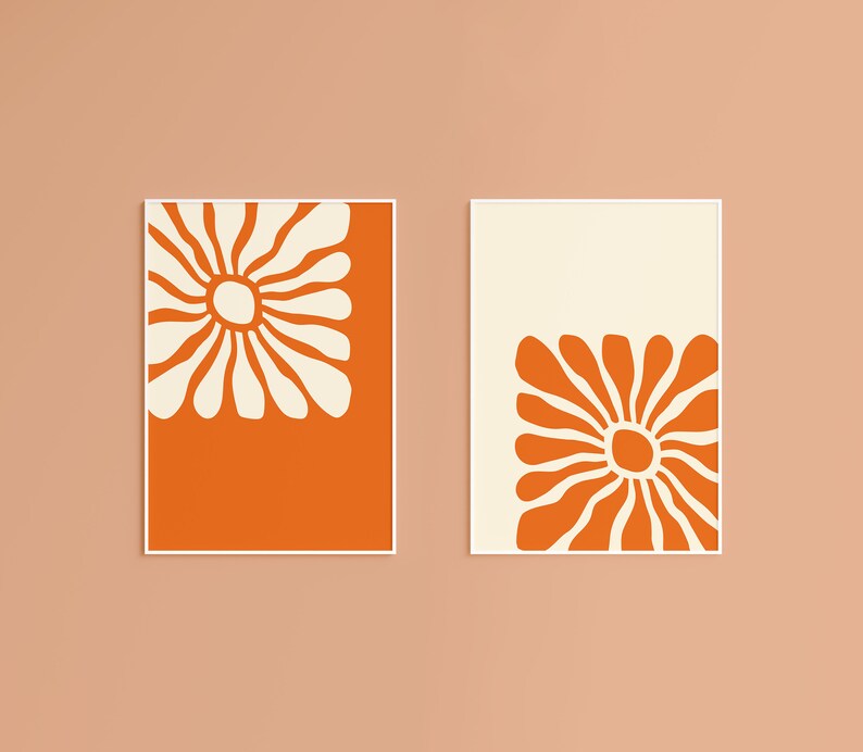 May include: Two framed prints with a white floral design on a bright orange background. The floral design is a stylized daisy with a large center circle.