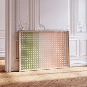 May include: A large framed print featuring a gradient of circles in shades of green, peach, and beige. The artwork is displayed against a white wall with ornate molding and rests on a wooden floor. The frame is a light wood color.