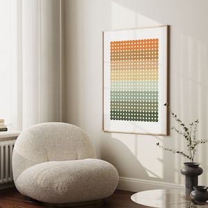 Op de afbeelding: Een ingelijst abstract print met een geometrisch patroon van oranje, bruine, gele, groene en blauwe cirkels. De print hangt aan een witte muur boven een beige fauteuil.