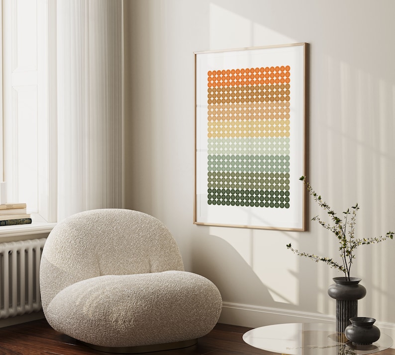 Op de afbeelding: Een ingelijst abstract print met een geometrisch patroon van oranje, bruine, gele, groene en blauwe cirkels. De print hangt aan een witte muur boven een beige fauteuil.