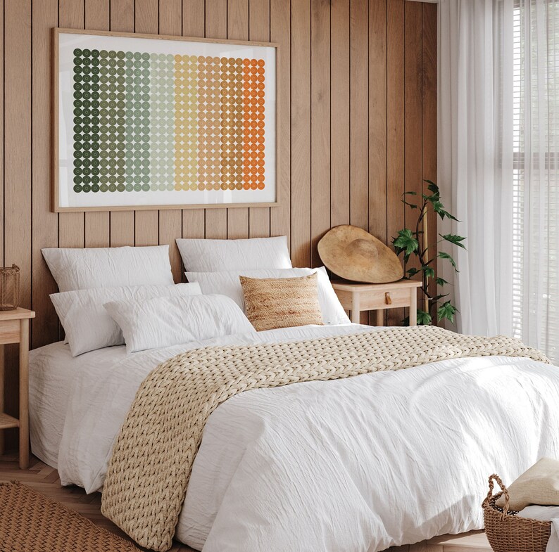 Op de afbeelding: Een wit bed met een beige gebreide deken en een geometrische print op de muur boven het hoofdeinde. Het bed is gestyled met witte kussens en een beige kussen met een geweven textuur.