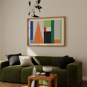 Może przedstawiać: Zielona welurowa sofa z czarno-białymi poduszkami, drewniany stolik z lampą i książką oraz oprawiony abstrakcyjny geometryczny obraz na ścianie nad sofą.
