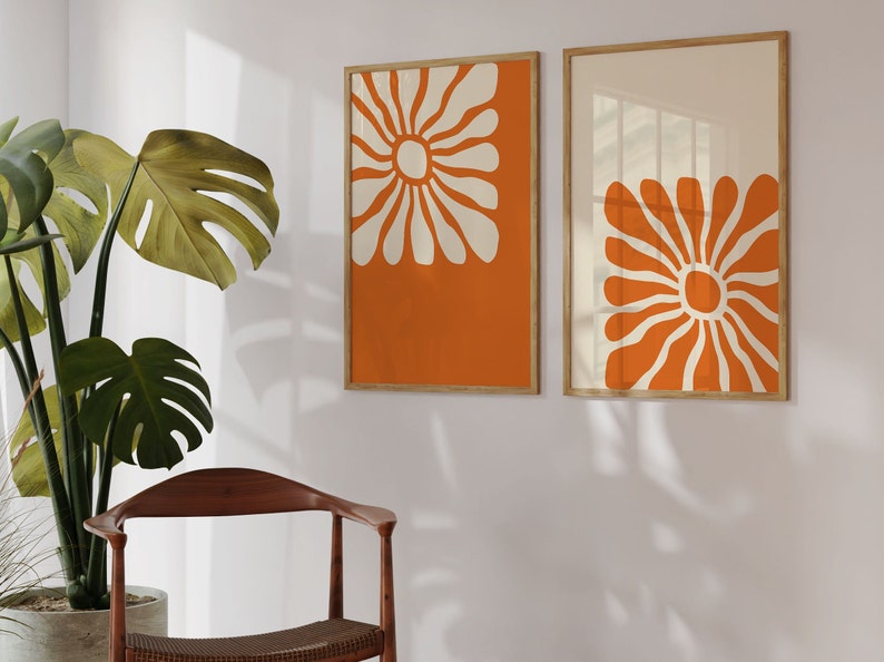 May include: Two framed prints with orange and white abstract floral designs. The prints are hung on a white wall.