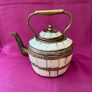 May include: A white and gold teapot with a brass handle and spout. The teapot is decorated with intricate patterns and has a copper lid.