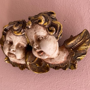 Könnte beinhalten: Ein Paar Cherubim-Engel mit goldenen Akzenten und Flügeln. Die Engel sind aus Holz geschnitzt und in einem Weiß- und Goldfarbschema bemalt.