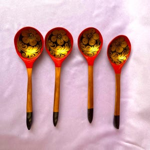 Könnte beinhalten: Vier Holzlöffel mit roten Schalen und Griffen. Die Schalen haben ein schwarzes und goldenes Blumenmuster. Die Griffe sind aus Naturholz mit schwarzen Spitzen. Diese dekorativen Löffel sind wahrscheinlich für die Präsentation oder das Servieren.