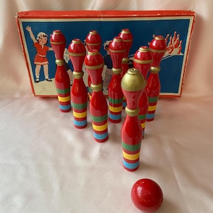 May include: A set of ten wooden bowling pins with red, yellow, green, and blue stripes. The pins are arranged in a triangle formation. A red wooden ball is in the foreground.