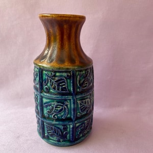 May include: A ceramic vase with a brown top and a teal and blue body. The body features a repeating pattern of square panels with leaf designs. The vase has a narrow neck and a flared opening, standing approximately 8 inches tall.