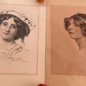 May include: Two black and white pencil drawings of women. The woman on the left is wearing a hat and a dress. The woman on the right is wearing a ribbon in her hair. Both drawings are framed.