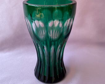 May include: A green glass vase with a fluted design. The vase has a wide opening and a flared base. The glass is a deep emerald green color, and the fluted design creates a textured effect. The vase is likely used for flowers or decorative purposes.