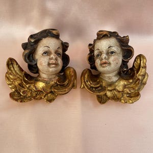 May include: Two antique wooden cherub angel wall decorations with gold leaf accents. The cherubs have painted faces and brown hair.