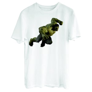 May include: White t-shirt with a green Hulk graphic. The Hulk is depicted in a dynamic pose, with his fists clenched and his face contorted in a fierce expression.
