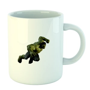 May include: White ceramic mug with a green Hulk character graphic. The Hulk is depicted in a dynamic pose, with his fists clenched and his face contorted in a fierce expression.