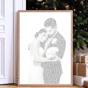 May include: A framed print featuring a silhouette of a person composed of text. The artwork is in a light brown wooden frame, with a white background. The print is displayed near a Christmas tree with ornaments and wrapped gifts.