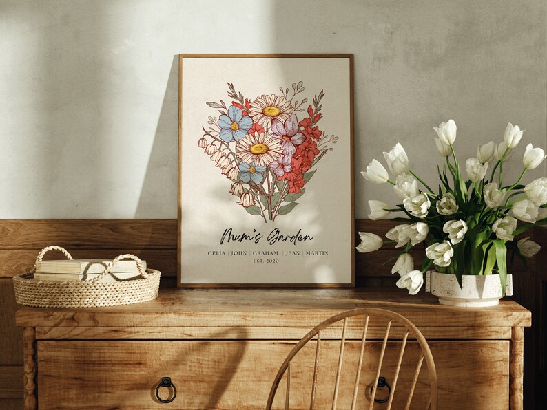 Personalised Mum's Garden birth flower bouquet print in a gold wood frame, styled on a rustic wooden sideboard next to a vase of fresh white tulips, hand-drawn botanical illustration featuring daisies, bluebells, lily of the valley and gladiolus in warm vintage tones, personalised with custom family names and established year, mothers day gift for mum