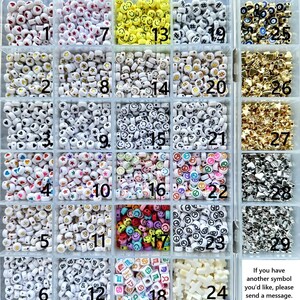 May include: A clear plastic storage container with twenty-nine compartments filled with various small plastic beads. The beads feature symbols including hearts, stars, smiley faces, peace signs, zodiac signs, and letters, labeled with numbers 1 through 29.
