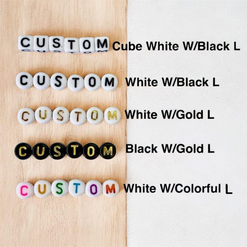 May include: Five rows of alphabet beads spelling CUSTOM. Row one: white cube beads with black letters. Row two: white round beads with black letters. Row three: white round beads with gold letters. Row four: black round beads with gold letters. Row five: white round beads with colorful letters.