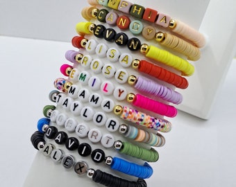 May include: A stack of colorful beaded bracelets with names spelled out in white letter beads. The bracelets feature various colors, including pink, yellow, green, and blue, with gold and silver accents. The names include Sophia, Candy, and others.